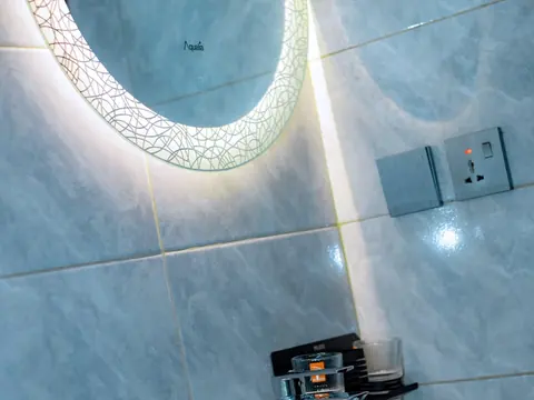 Illuminated round bathroom mirror above a tap and tiled wall