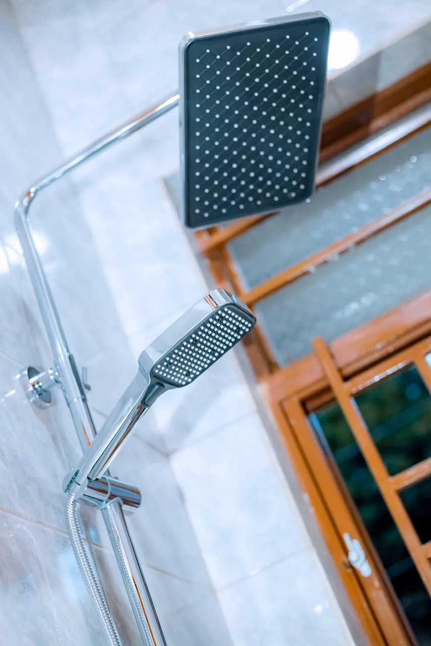 Square overhead shower head and handheld shower against a tiled wall