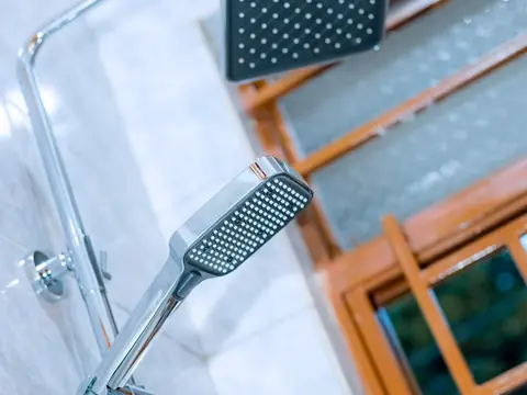 Square overhead shower head and handheld shower against a tiled wall