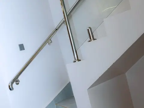 Indoor staircase with pale steps, a glass balustrade and metal handrail